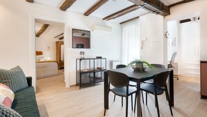 Ein modernes Wohnzimmer mit Essbereich, Holzbalken an der Decke, einer Couch, einem Esstisch mit Stühlen und einer Küche im Hintergrund.