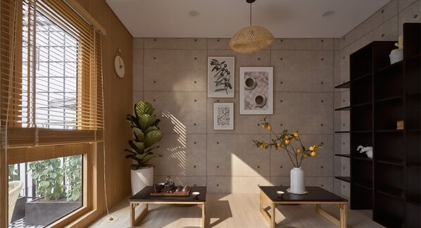 Una habitación moderna con un ventanal grande, una planta en maceta, una mesita con bandeja y una pared decorada con cuadros.