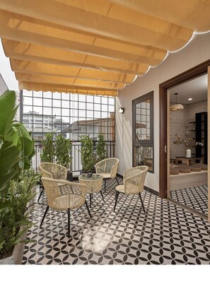 A balcony with wicker furniture, potted plants, and a patterned floor. - The First May (Hanoi)