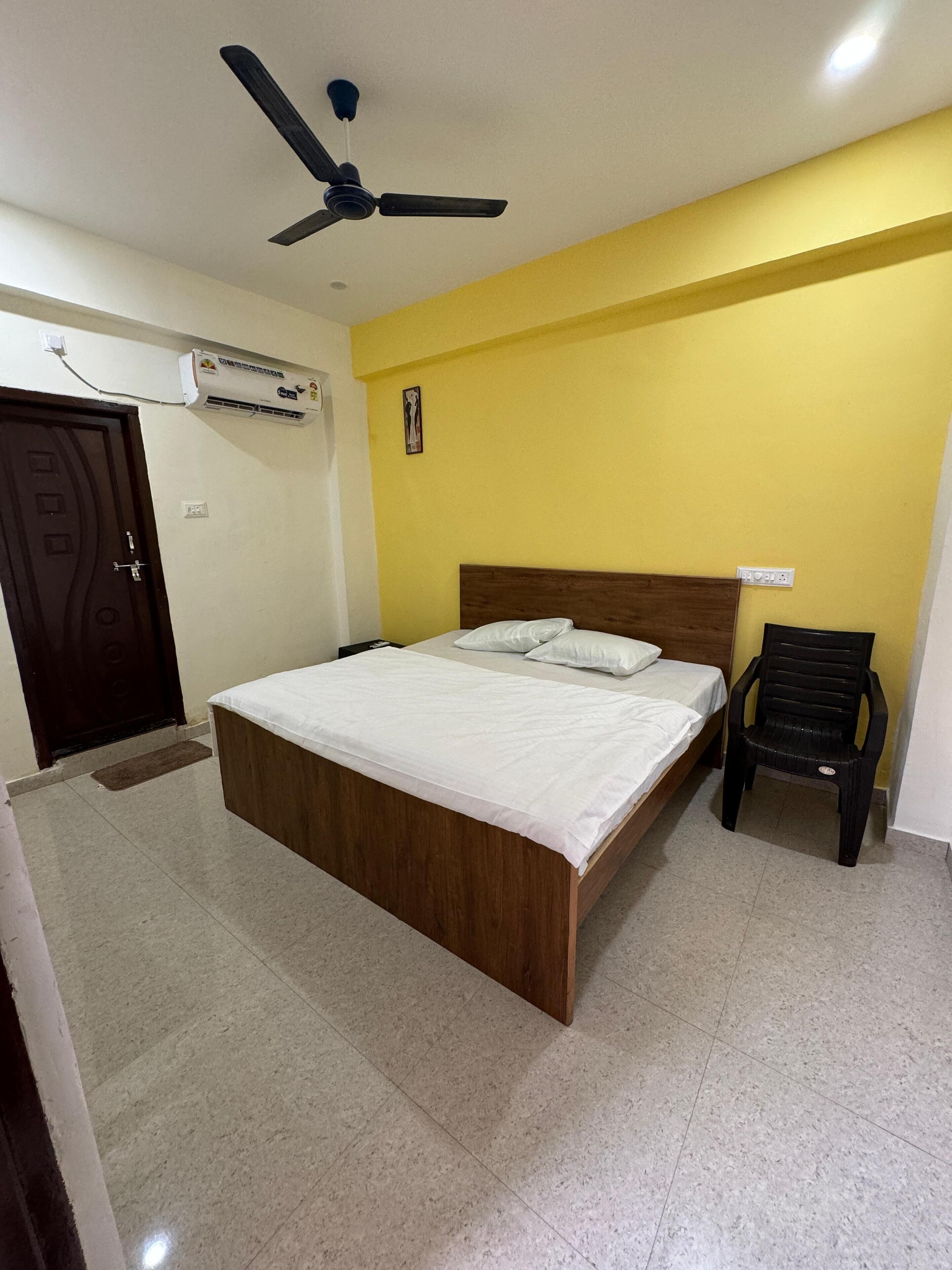 Une chambre avec un lit, un ventilateur de plafond, un appareil de climatisation et une chaise.