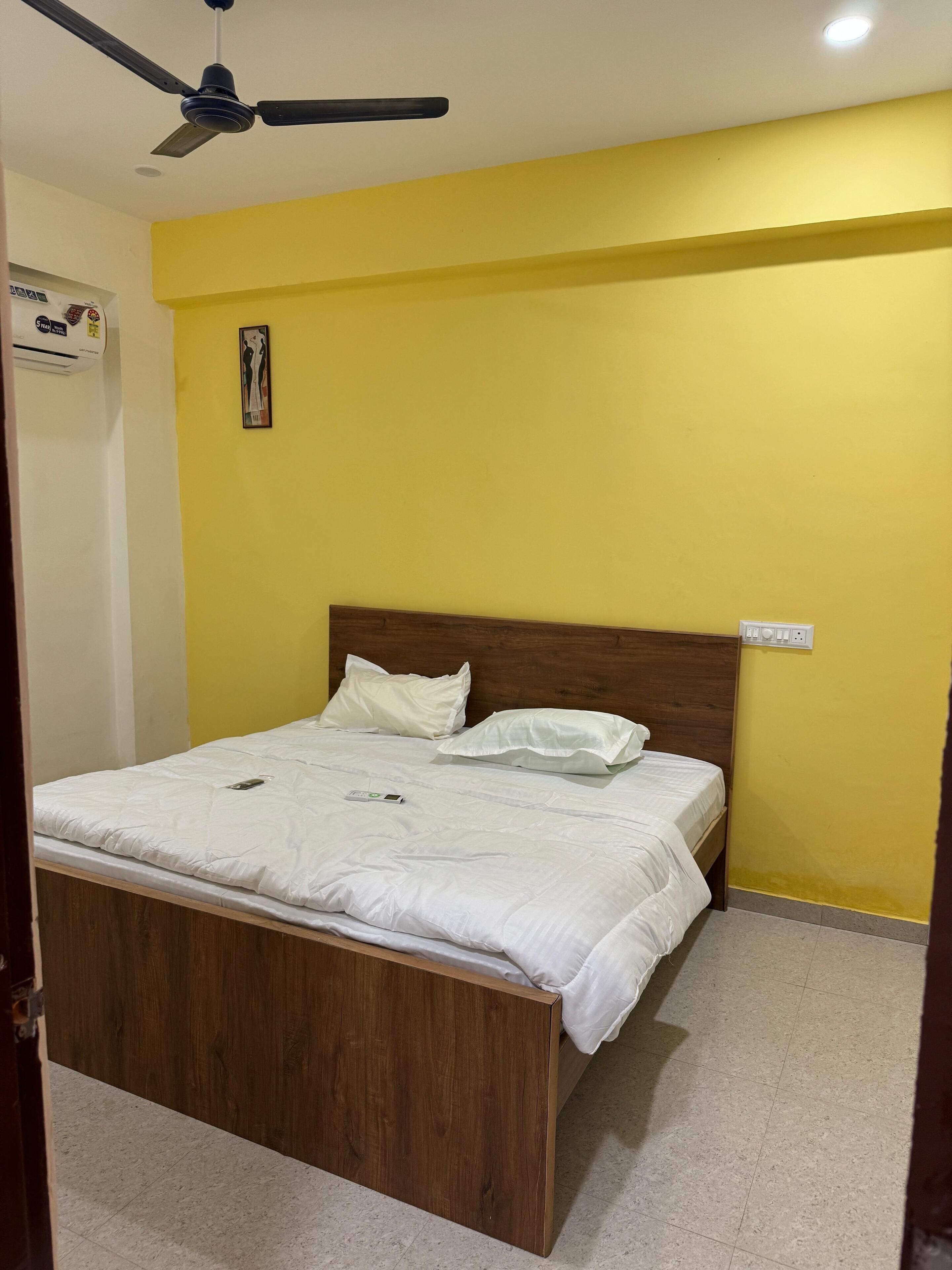 Ein Schlafzimmer mit einem hölzernen Bett, weißer Bettwäsche, einem Deckenventilator und einer gelben Wand.