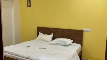 Ein Schlafzimmer mit einem hölzernen Bett, weißer Bettwäsche, einem Deckenventilator und einer gelben Wand.