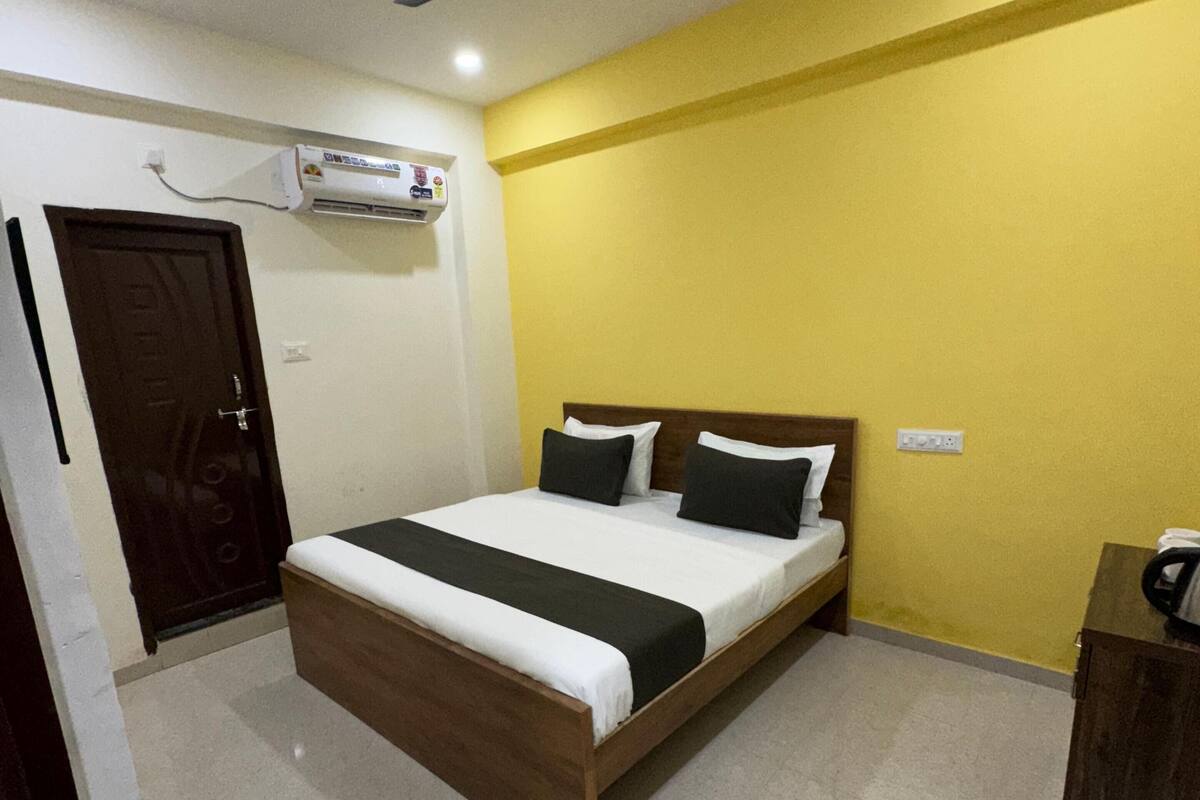 A bedroom with a bed, a ceiling fan, an air conditioning unit, and a wooden wardrobe.