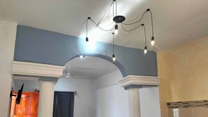 Un soggiorno con divano, tavolino e TV a parete. Si nota una porta in legno e un frigorifero nella stanza.