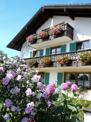 Traditional alpine-style building with a balcony overlooking a lush garden.