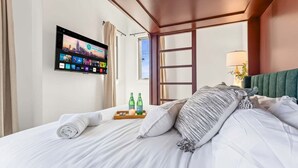 A hotel room with a bed, a flat-screen TV mounted on the wall, a window, and a nightstand with bottles and a tray. - Nashville house near Geodis Park with hot tub, game room, sleeps 12 (Nashville)