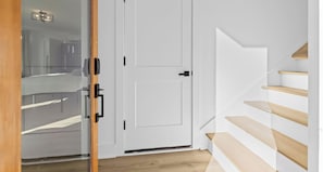 A modern interior with a white door, a glass partition, and a wooden staircase.