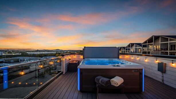 A rooftop terrace with a hot tub, wooden deck, and string lights.