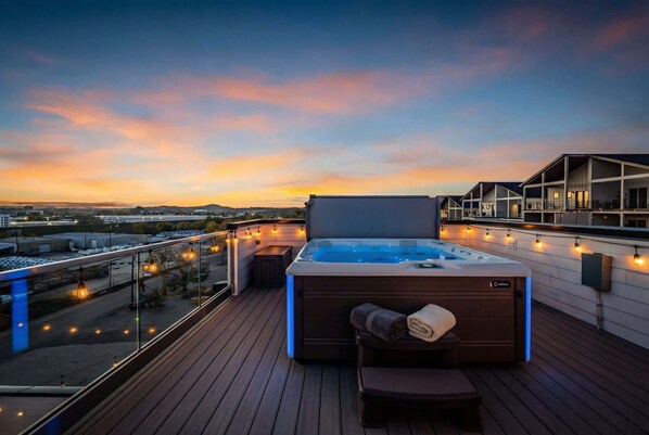 A rooftop terrace with a hot tub, wooden deck, and string lights.