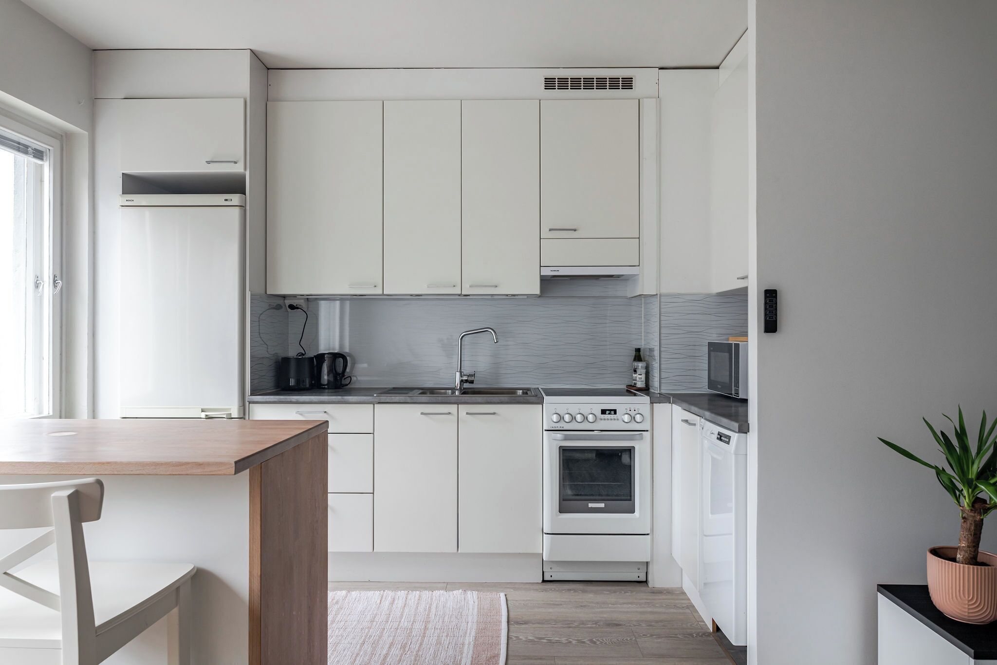 A modern kitchen with white cabinets, a built-in oven, a microwave, and a sink.