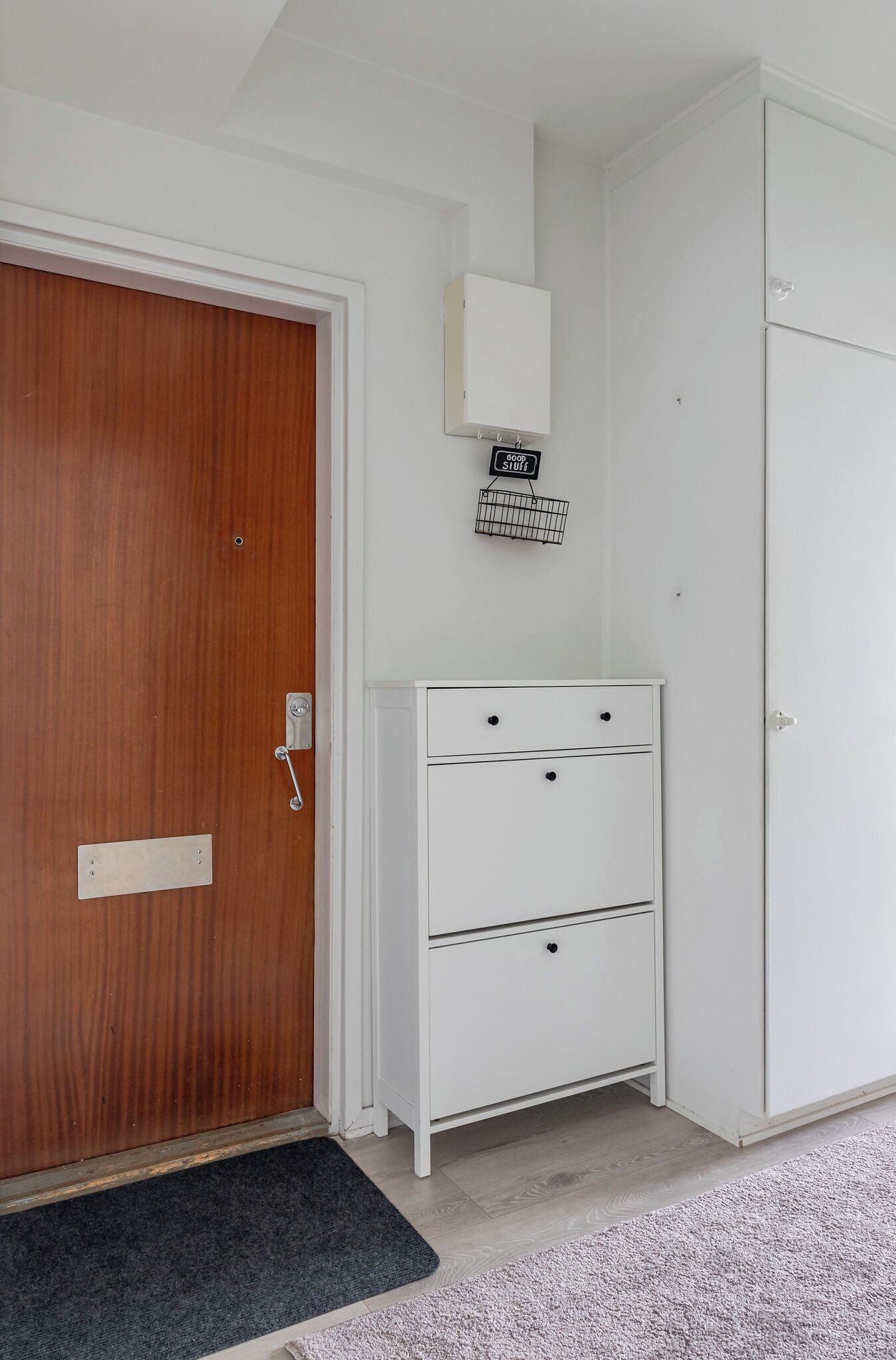 A room with a wooden door, a white cabinet with drawers, and a small sign above it.