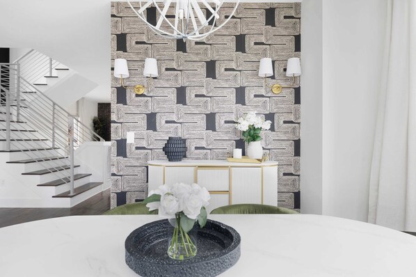 A modern interior with a geometric patterned wall, a white staircase, and a round table with a vase of flowers.