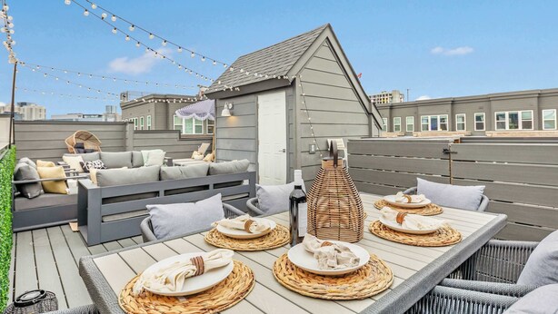 Une terrasse sur le toit, avec une table à manger pour quatre personnes, entourée de chaises en osier et d’un petit coin salon agrémenté de coussins.