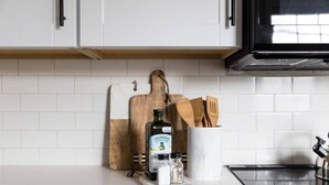 A kitchen counter with a cutting board, a bottle of olive oil, salt and pepper shakers, and wooden utensils. - Harmonic & Songbird Bungalows - 2, 2 bedrooms! (Nashville)