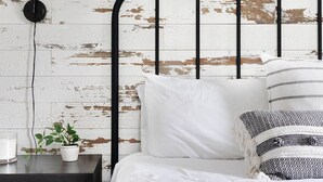 A bed with a black metal headboard, white bedding, and a grey quilted blanket. There is a bedside table with a lamp and a potted plant. - Harmonic & Songbird Bungalows - 2, 2 bedrooms! (Nashville)