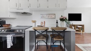 Una cocina moderna con armarios blancos, horno empotrado y una zona de bar con dos taburetes.