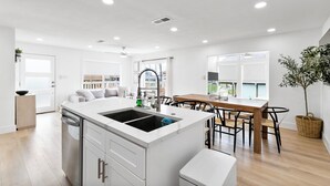 Une cuisine moderne dotée d’un îlot central, de meubles blancs et d’un coin repas avec une table et des chaises en bois.