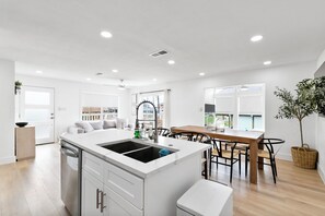 Una cucina moderna con isola centrale, mobili bianchi e zona pranzo con tavolo e sedie in legno.