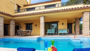 Ein Poolbereich mit Liegestühlen, einem Tisch mit Obst und einer überdachten Terrasse mit Sitzgelegenheiten.