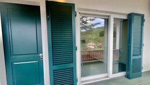 A teal-colored door with a window, a sliding glass door, and a balcony with a railing. - Casa San Michele a Bagnaia (Portoferraio)