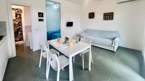A compact living space with a dining area, a kitchenette, a sofa, and a ceiling fan. - Casa San Michele a Bagnaia (Portoferraio)