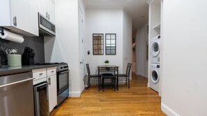 Une cuisine compacte dotée d’appareils électroménagers modernes, un coin repas avec une table et des chaises, et un lave-linge dans la pièce adjacente.