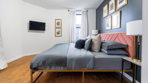 Une chambre à coucher avec un lit, une télévision, une fenêtre avec des rideaux et des tableaux encadrés accrochés au mur.