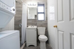 A compact bathroom with a white toilet, a sink, and a shower area. - Elegant Harlem Suites (New York)