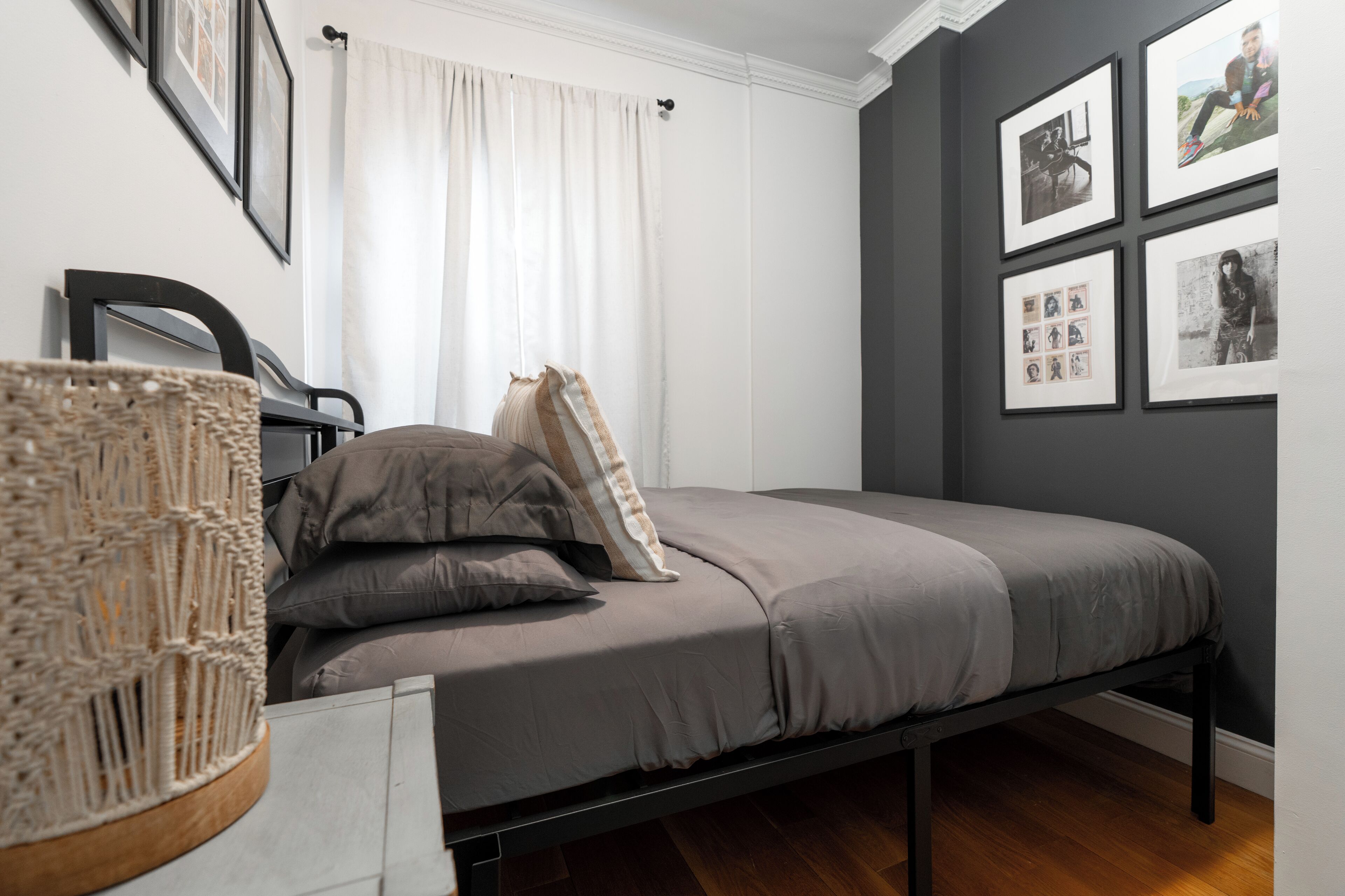 Une chambre à coucher avec un lit, une chaise, un panier en osier et des tableaux encadrés accrochés au mur.