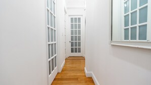 Un couloir étroit aux murs blancs et au plancher en bois, qui mène à une porte dotée de panneaux en verre dépoli.