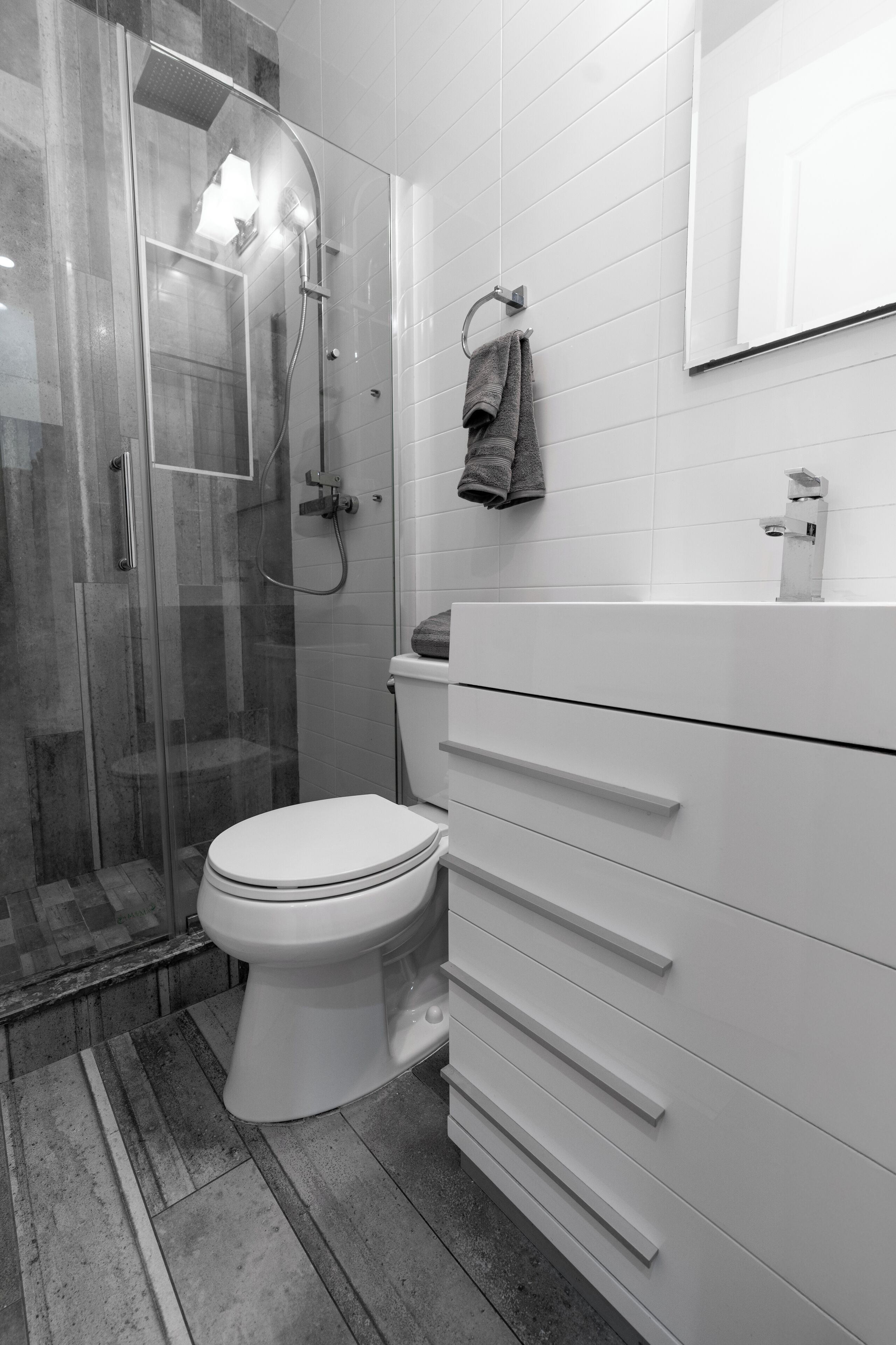 Une salle de bain moderne avec une douche à parois de verre, des toilettes blanches et un meuble-lavabo avec des tiroirs.