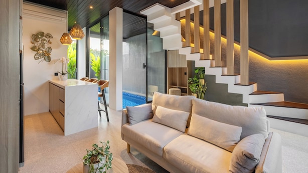 A modern living room with a sofa, a kitchen area, and a staircase with integrated lighting. - Private Villa Ayra 8D 10min MelastiBeach (Ungasan)