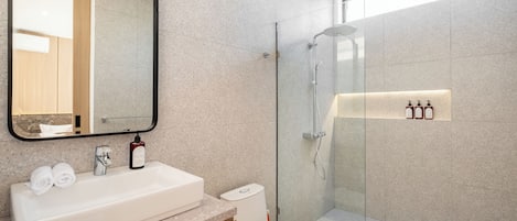 Un baño moderno con un lavamanos grande, inodoro y ducha con mampara de vidrio.