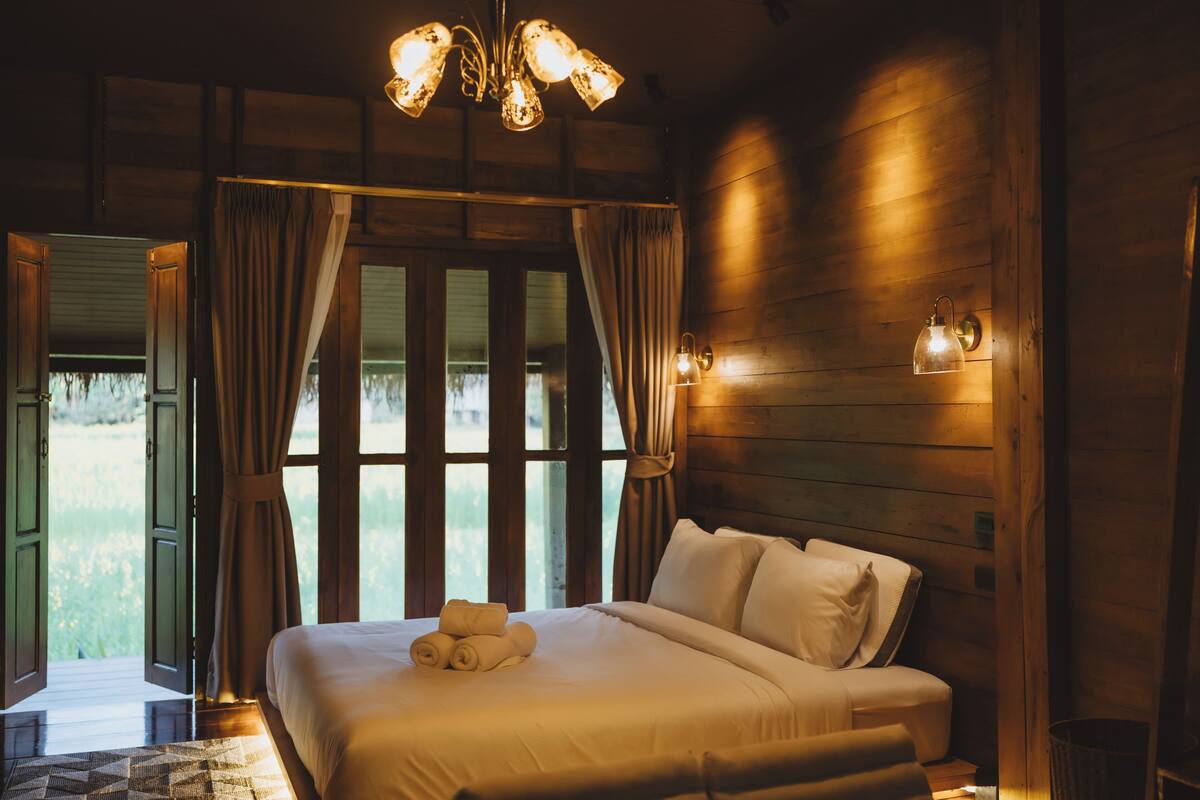 A wooden room with a bed, curtains, and a window.