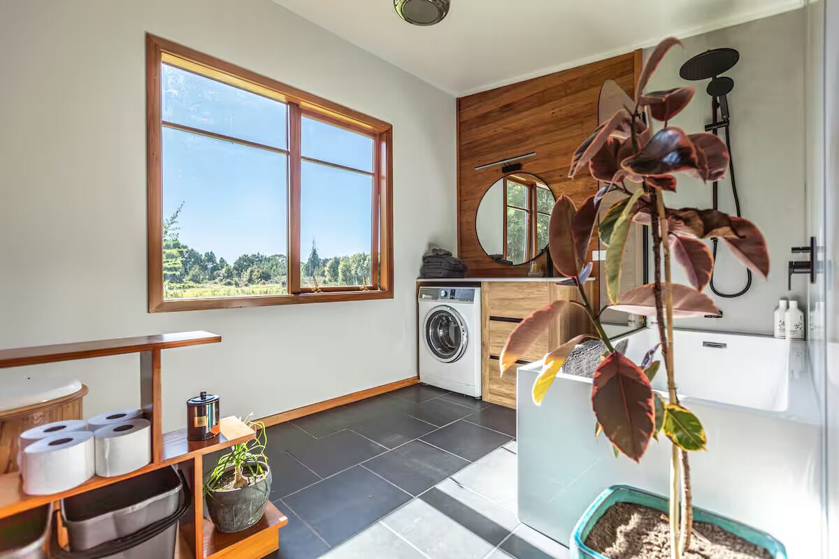 A modern kitchen with a large window, a washing machine, and a potted plant.