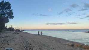 A beach with a rocky shore, a few trees, and two people fishing. - The Piggery (Parapara)