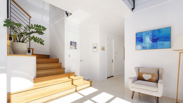 A modern interior with a wooden staircase, a white armchair with a heart-shaped pillow, and a blue abstract painting on the wall.