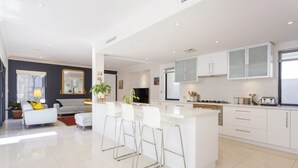 A modern kitchen with white cabinetry, a central island with bar stools, and a dining area with a sofa and coffee table.