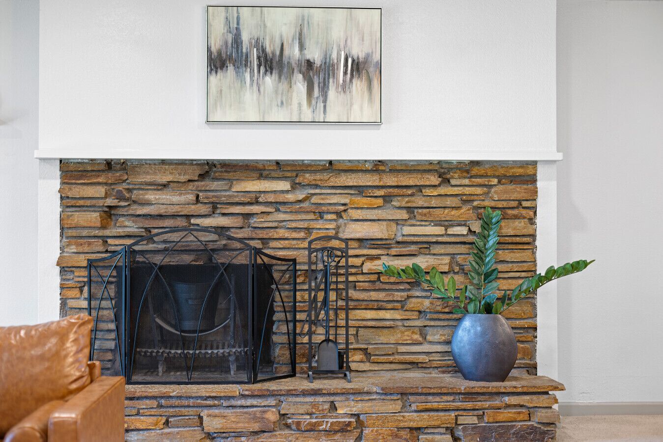 A stone fireplace with a metal screen, a potted plant, and a framed abstract painting on the wall.