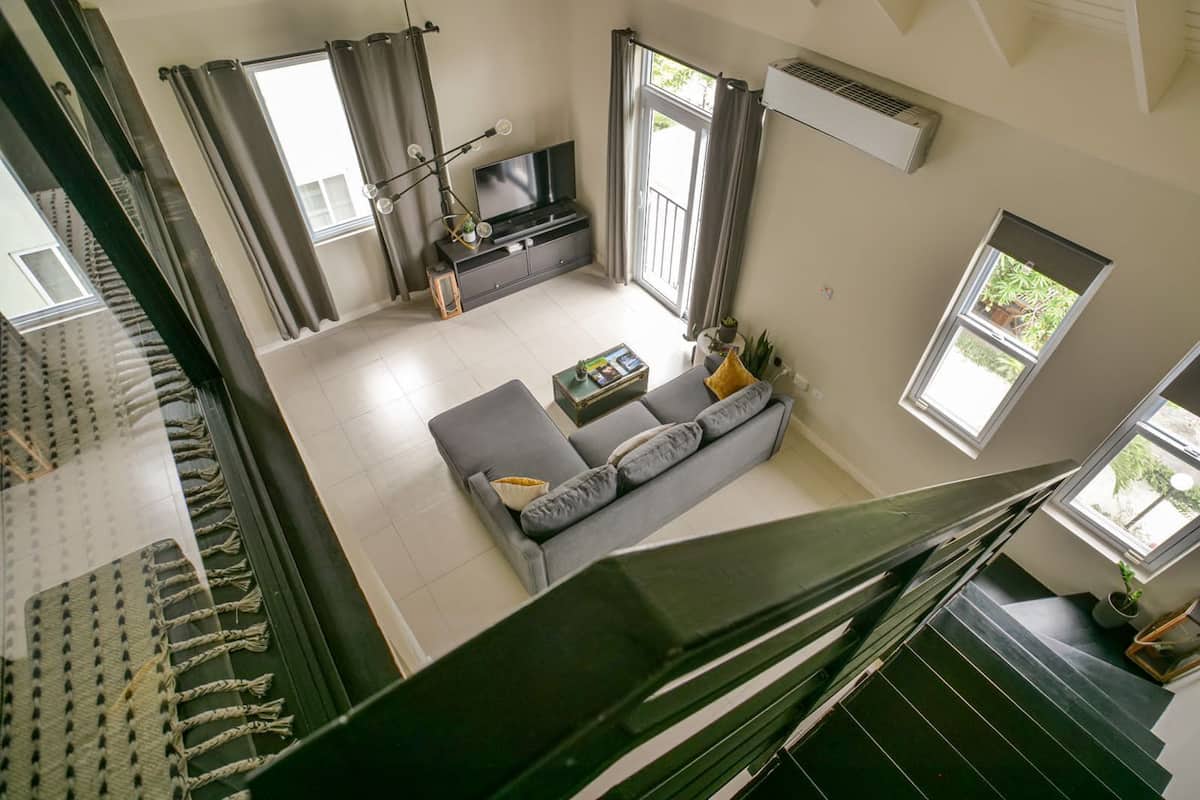 Una sala de estar moderna con un sofá gris, un televisor de pantalla plana y una escalera que conduce a un piso superior.