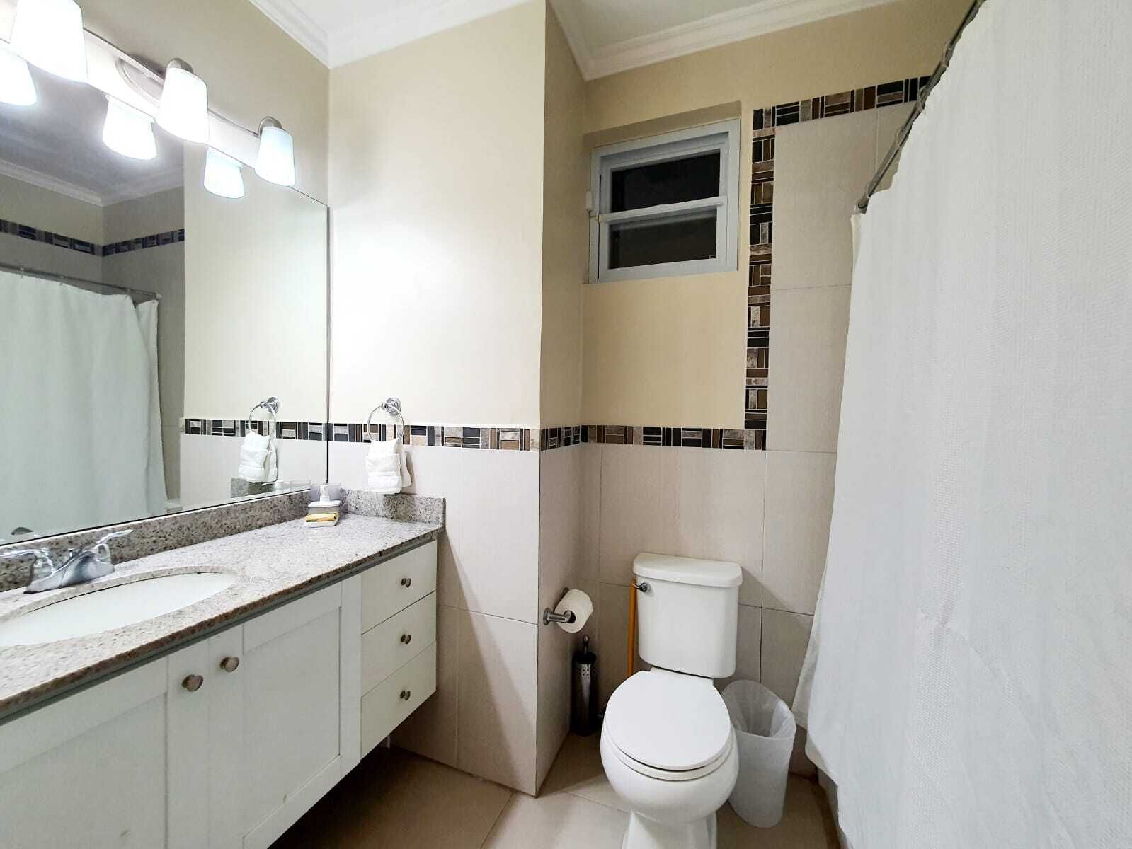 A bathroom with a sink, mirror, toilet, and shower curtain.