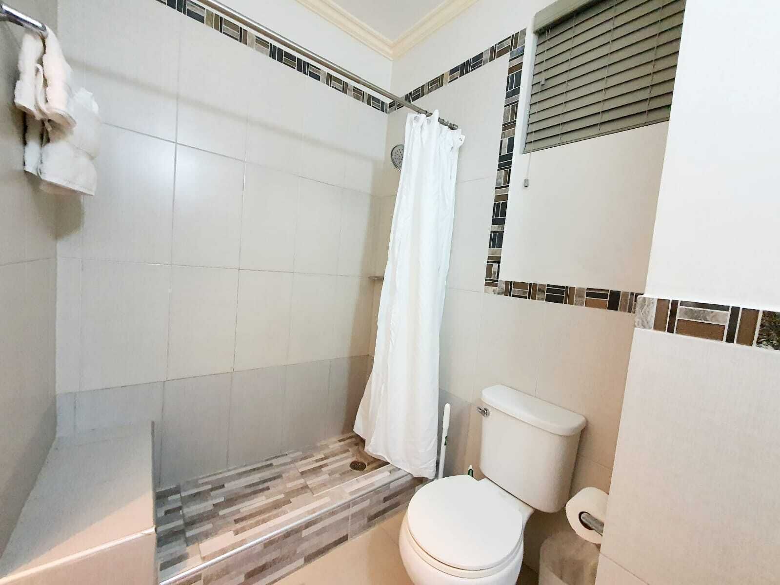 A bathroom with a shower, toilet, and a tiled floor.