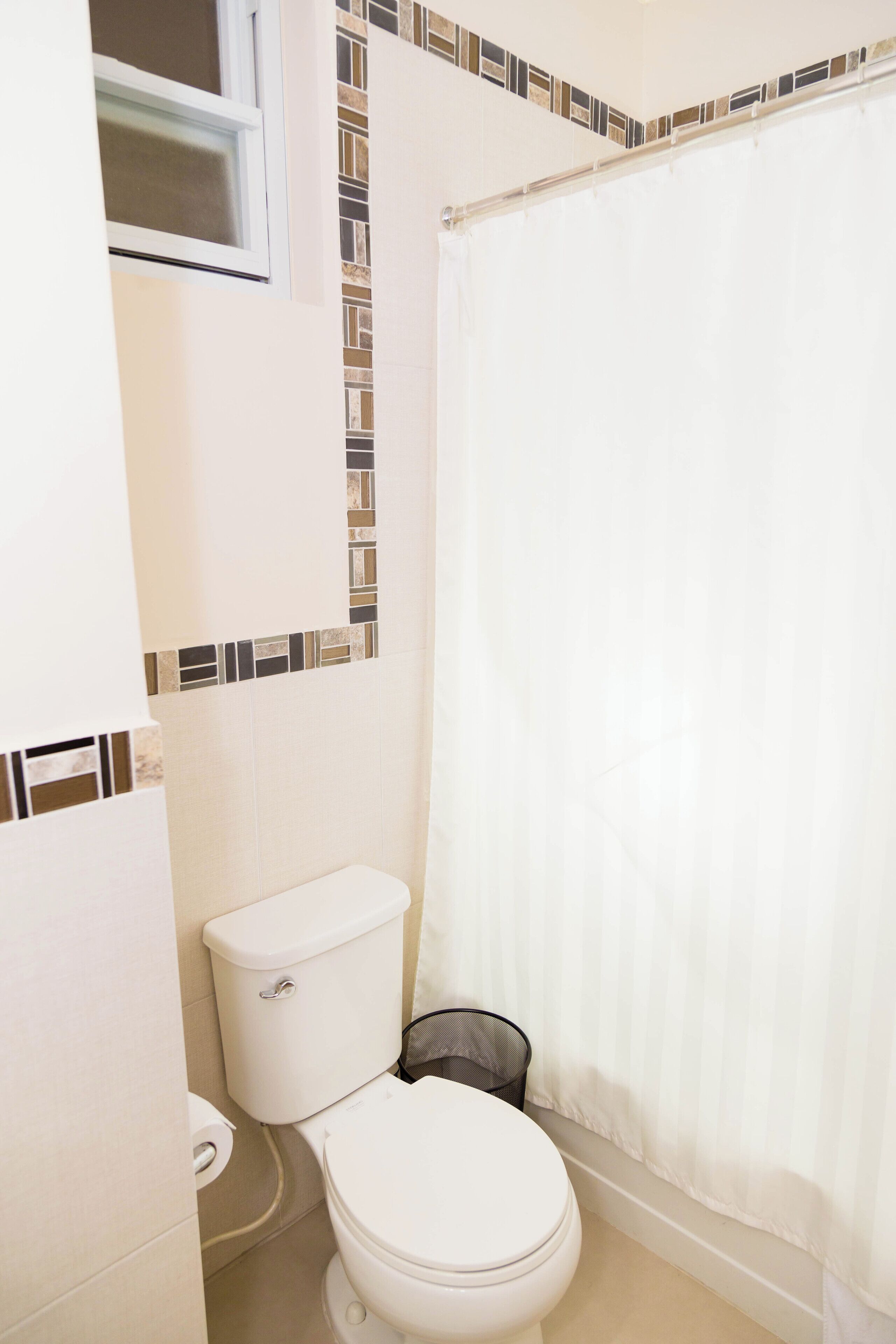 Une salle de bain avec des toilettes, un rideau de douche et une fenêtre.