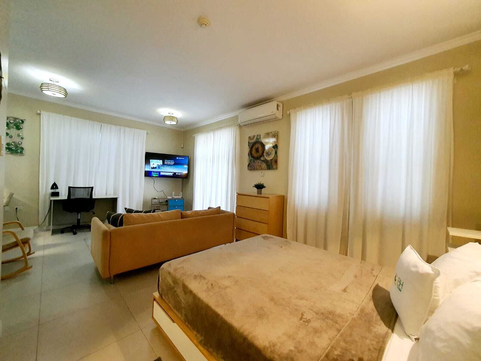 A hotel room with a bed, a sofa, a desk with a computer, and a TV.