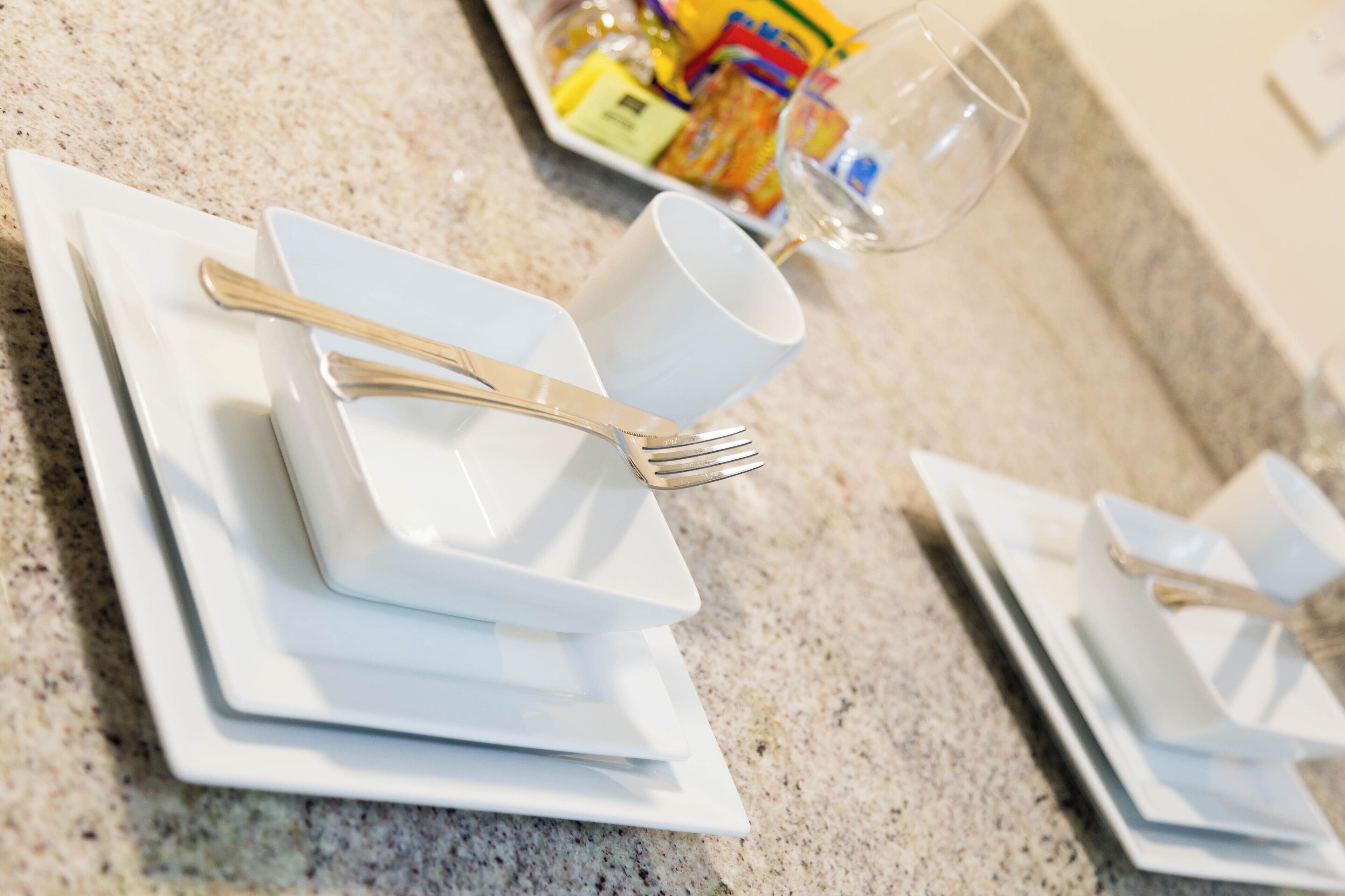 Ein ordentlich gedeckter Tisch mit weißen Tellern, einer Tasse und Besteck auf einer Granit-Arbeitsplatte.