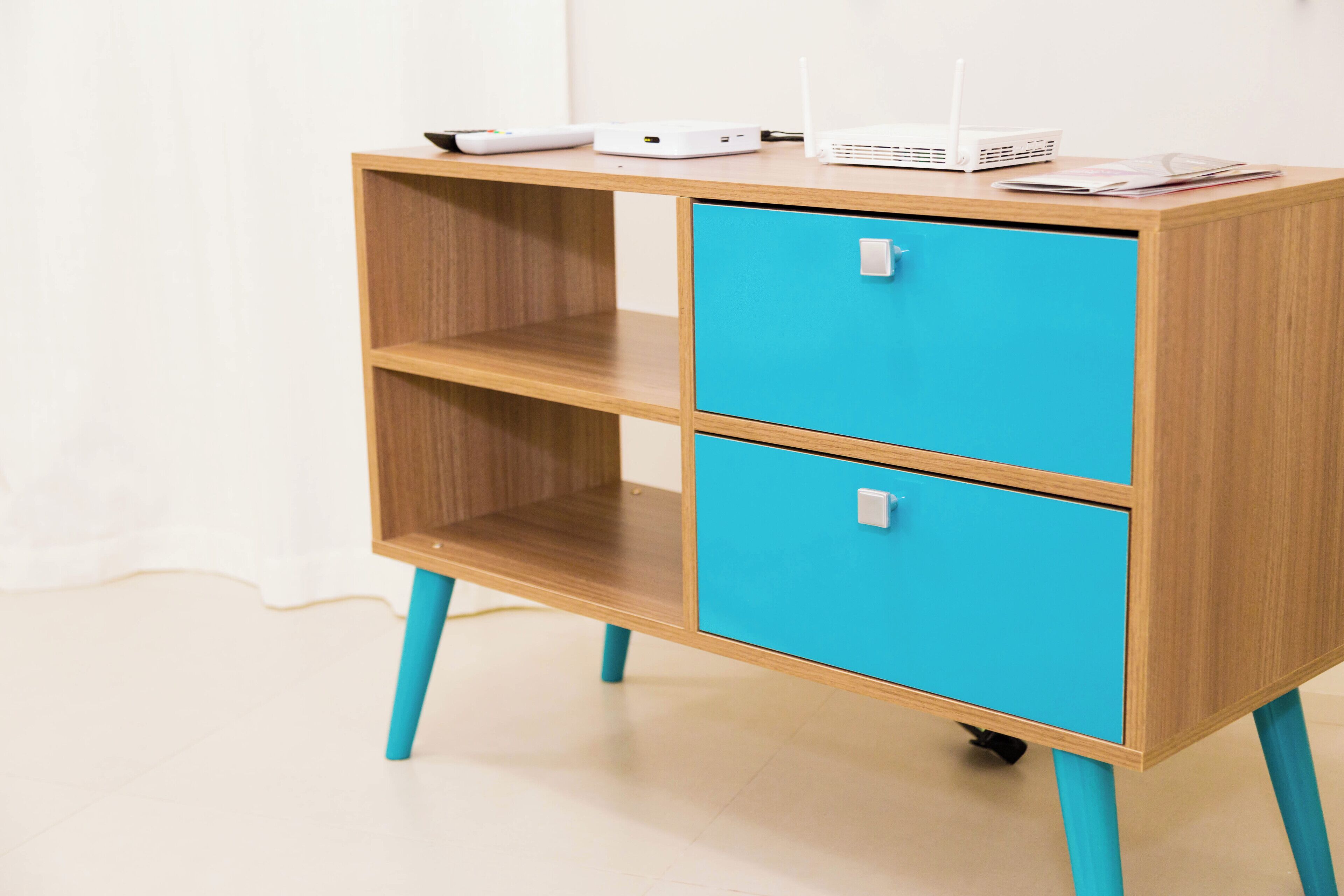 A wooden desk with two turquoise drawers and a shelf, featuring a router and a tablet on top.