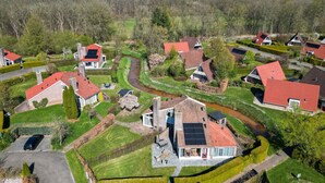A residential area with houses featuring red roofs, a winding road, and a river. - Kievit | Ruime bungalow met fijne tuin (Zwiggelte)