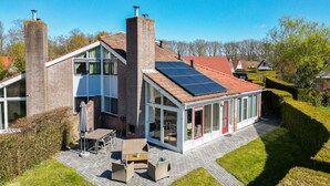 A modern house with a brick chimney, solar panels, and a patio with outdoor furniture. - Kievit | Ruime bungalow met fijne tuin (Zwiggelte)