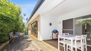 A covered patio with a wooden deck, outdoor seating, and a table with chairs. - Wiltons Riverside family haven, pet friendly (Ocean Grove)