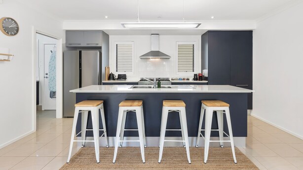 A modern kitchen with a central island, bar stools, a stainless steel refrigerator, and a hanging light fixture. - Wiltons Riverside family haven, pet friendly (Ocean Grove)